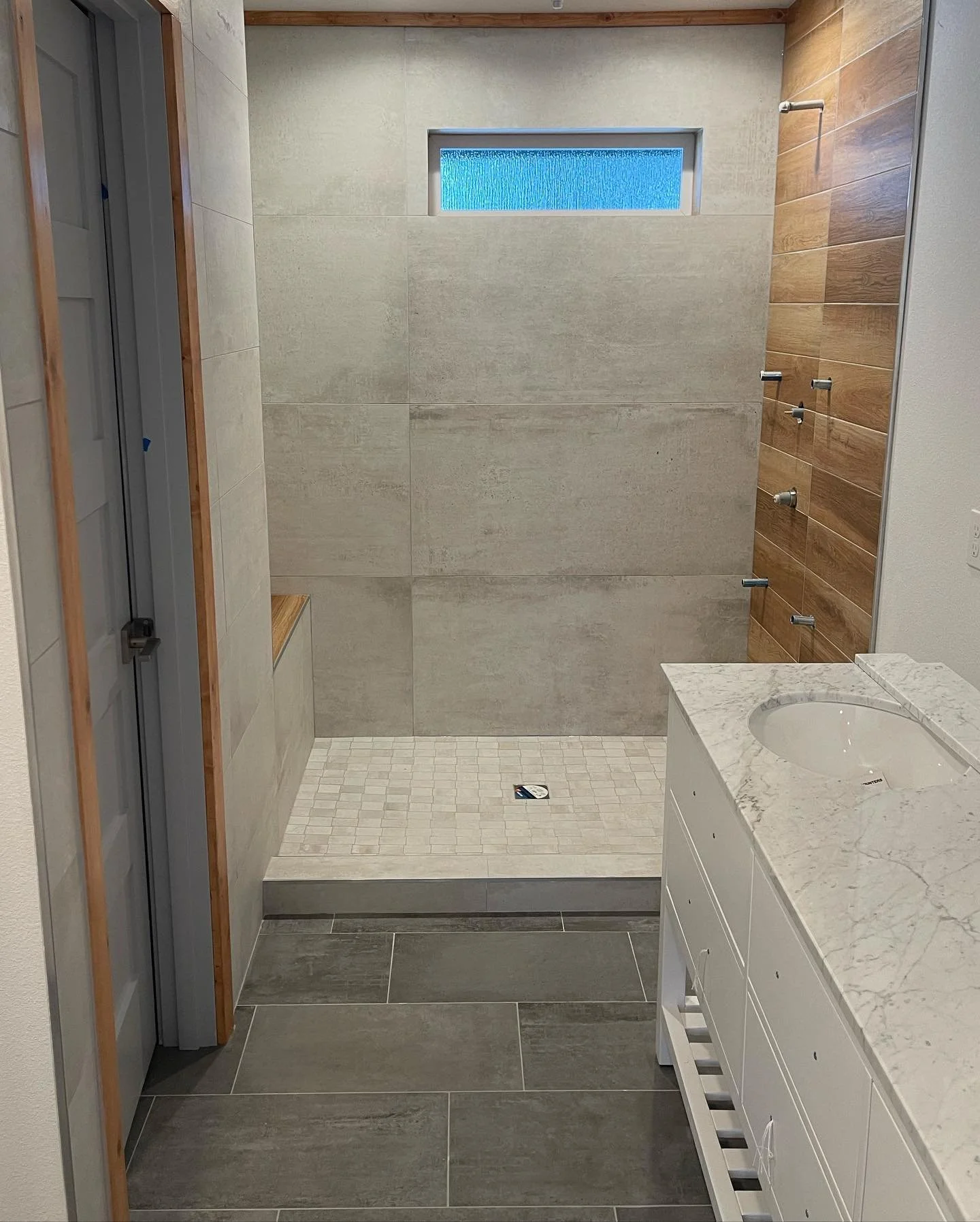 Bathroom with walk-in shower, wood accent wall and marble vanity
