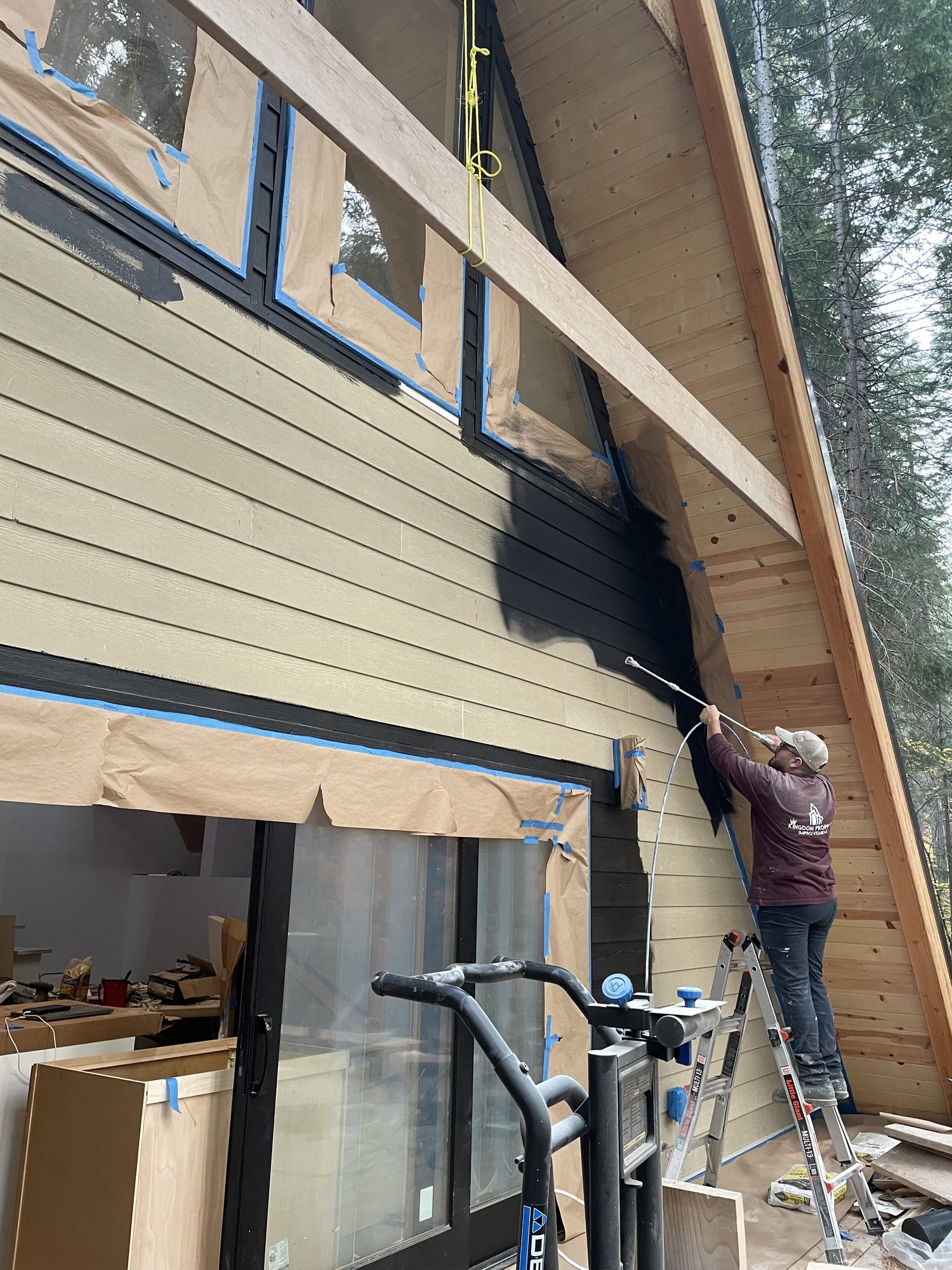 Painter on a ladder coating a home exterior in black