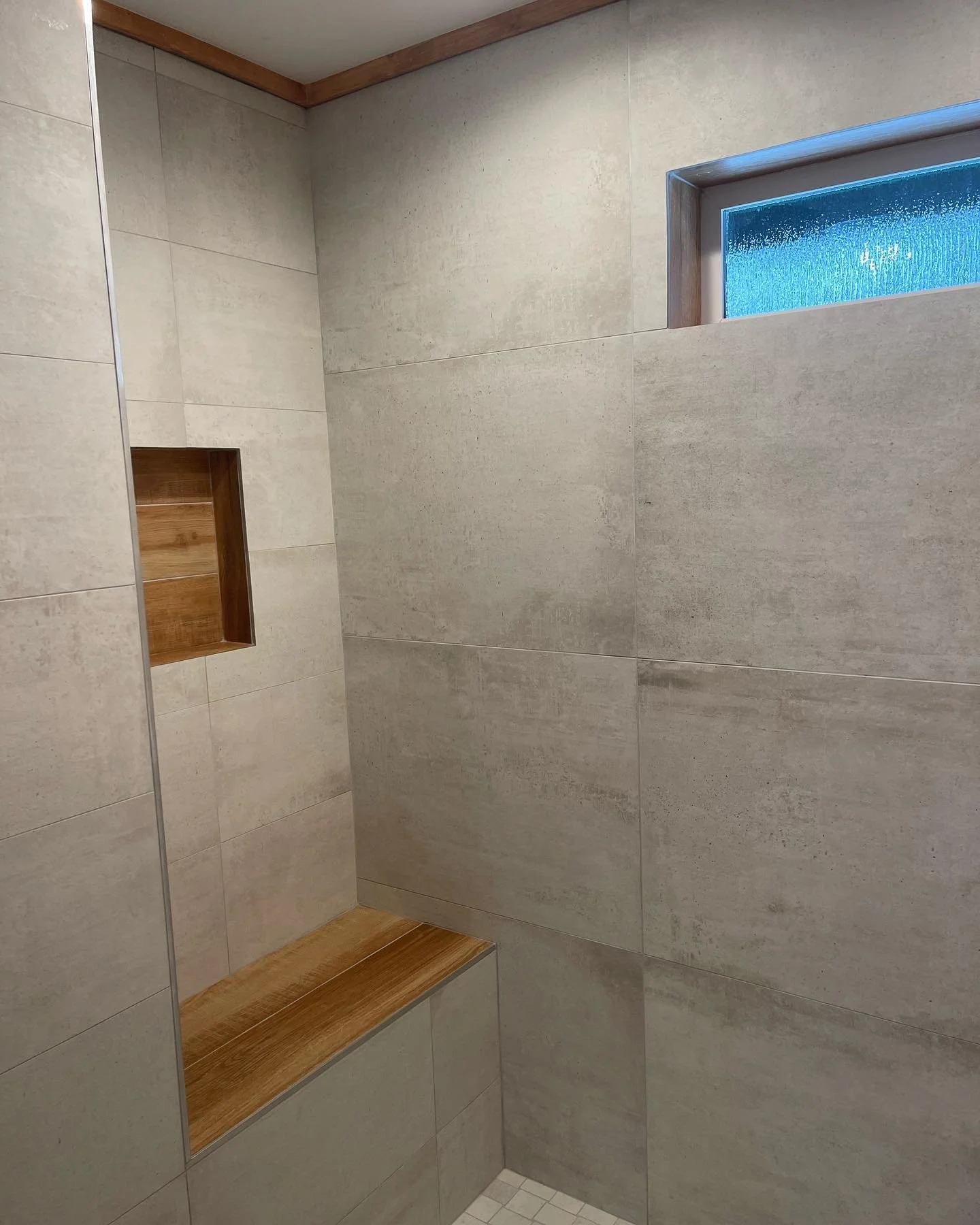 Shower with beige tile walls, glass block window and built-in wooden shelves